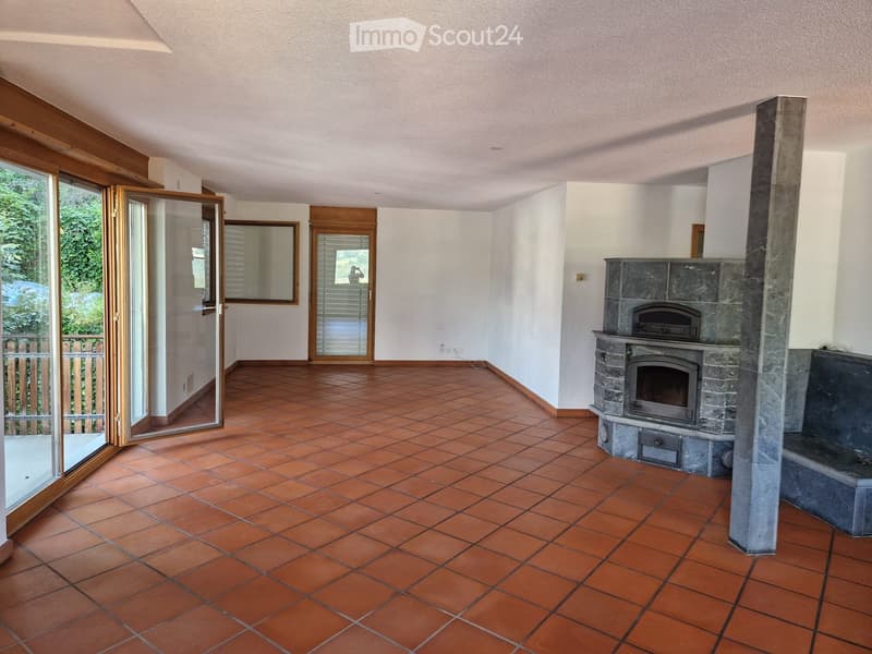 Living room with terracotta tiled floor, white walls, and a stone fireplace with a wood-burning stove.