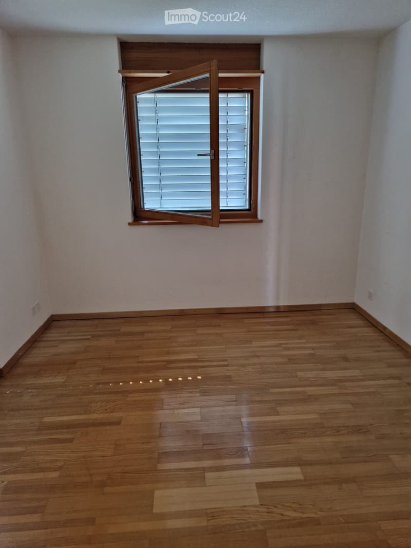 Empty room with wooden flooring and a single window with blinds.