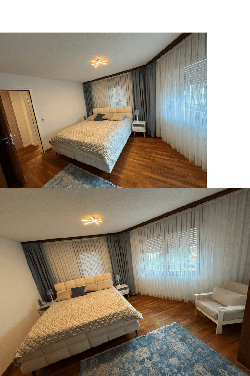 Spacious bedroom with wooden flooring, large windows with curtains, a bed with pillows and a quilt, a nightstand, a chair, and a decorative rug.