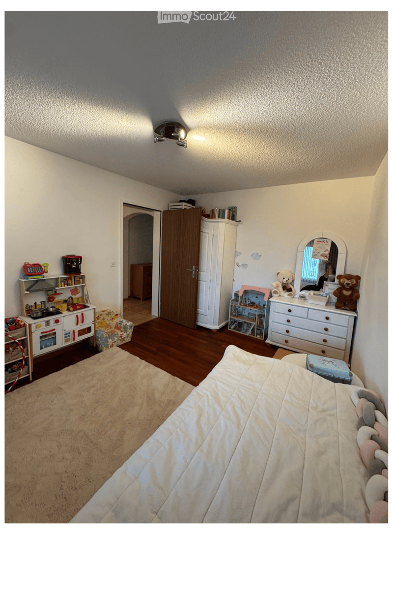 A well-lit children's bedroom with a bed, wardrobe, mirror, toy kitchen, and various toys.