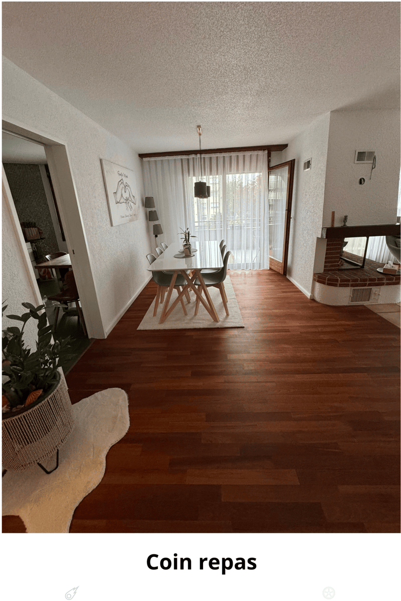 Dining room with wooden flooring, a modern dining table with chairs, a potted plant, a mirror, and artwork on the wall. The room features large windows with sheer curtains and a view of the outdoors.