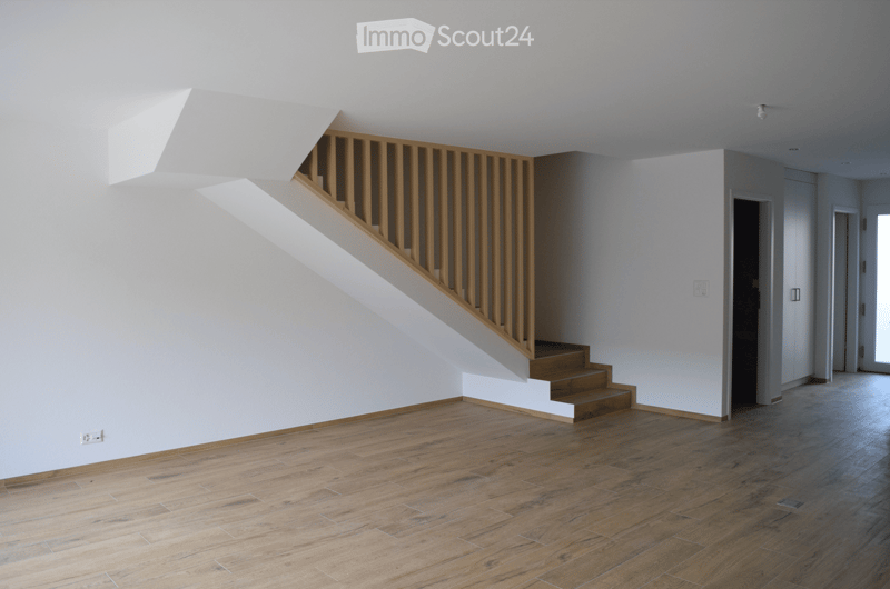 Empty room with wooden flooring, white walls, and a staircase leading upwards. No furniture or equipment is present.