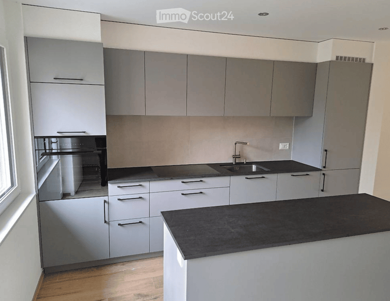 Modern kitchen with white cabinets, black countertops, and stainless steel appliances including an oven and sink.