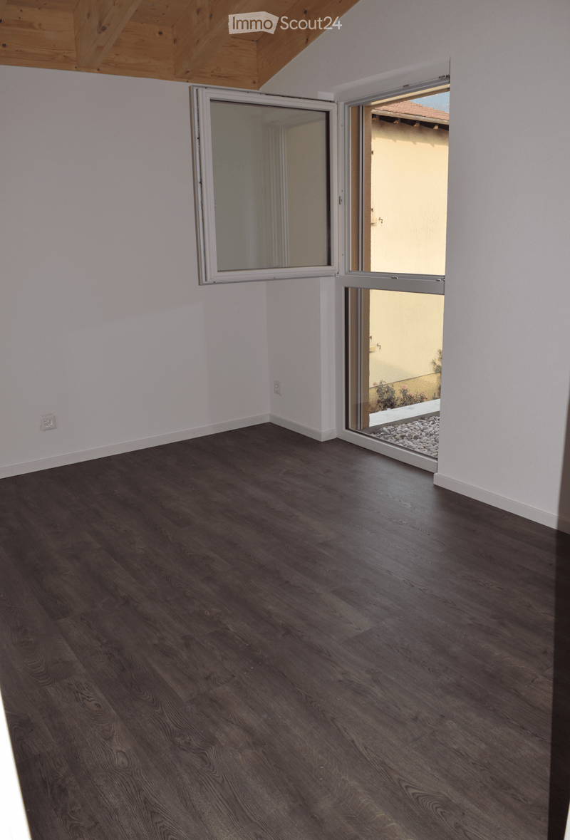 Empty room with dark wooden flooring, white walls, and large sliding glass doors leading to an outdoor area.