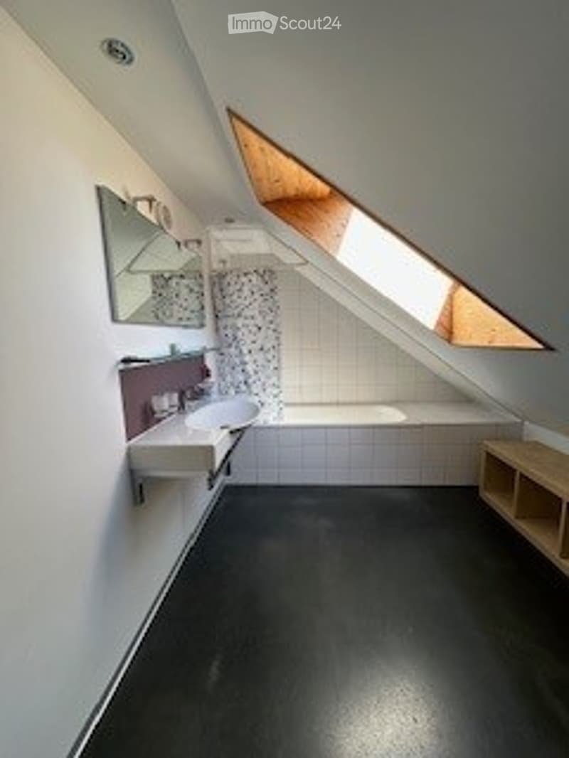 Modern bathroom with white tiled walls, black floor, a sink with a mirror, a bathtub with a shower curtain, and a wooden shelf.