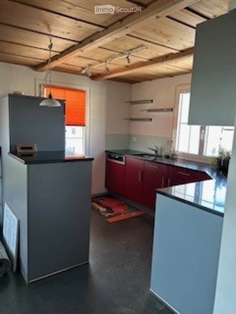 Modern kitchen with wooden ceiling beams, stainless steel appliances, red cabinets, and a black countertop.