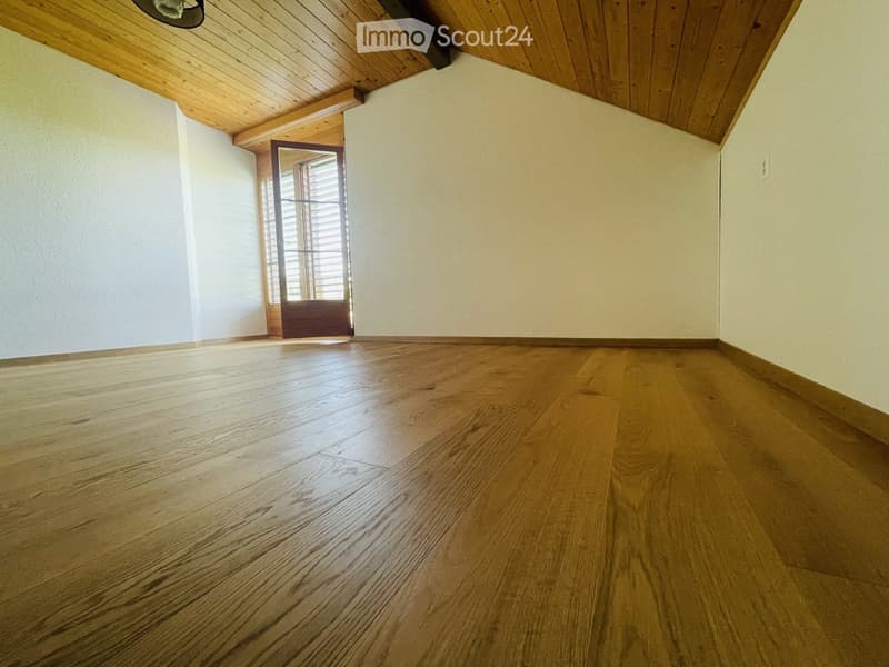 Empty room with wooden flooring, white walls, and a wooden door leading to another space.