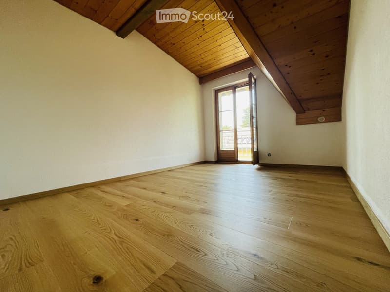 Empty room with wooden flooring and white walls, featuring a wooden ceiling and an open door leading outside.