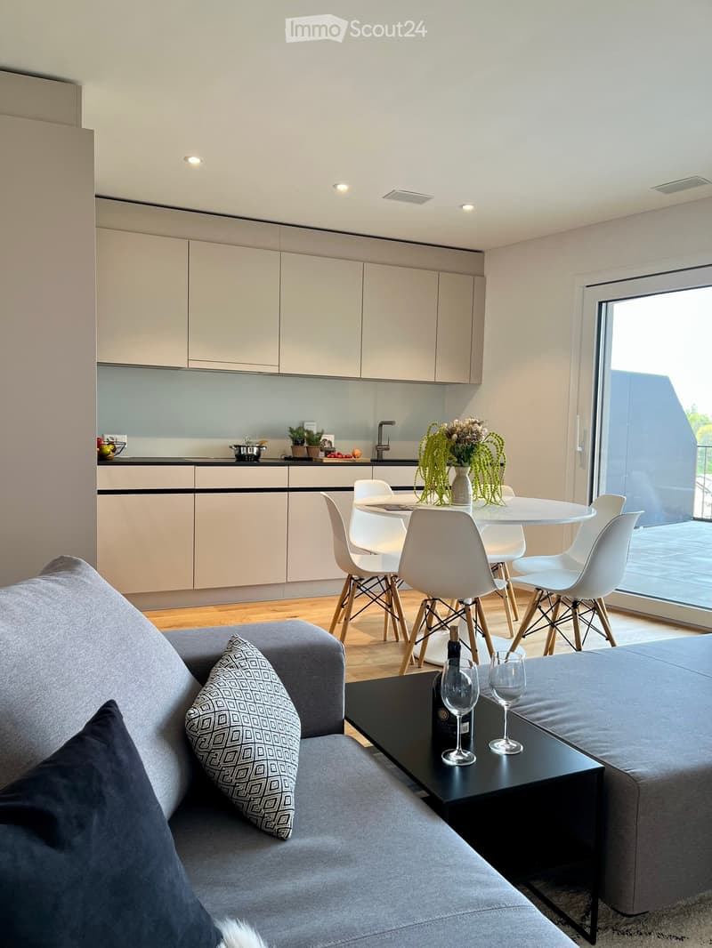 Modern living and dining area with a grey sofa, coffee table, dining table with chairs, and kitchen cabinets.