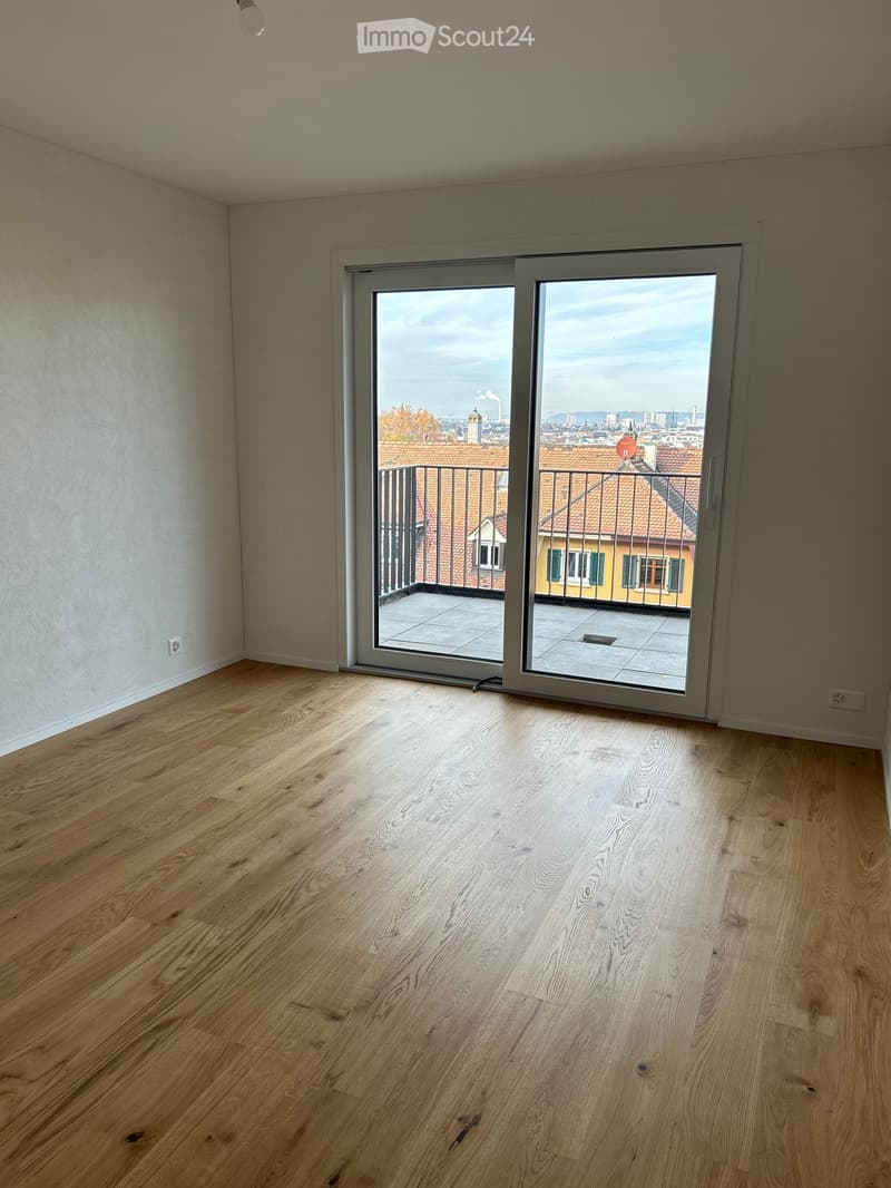 Empty room with wooden flooring and large sliding glass doors leading to a balcony with cityscape view.