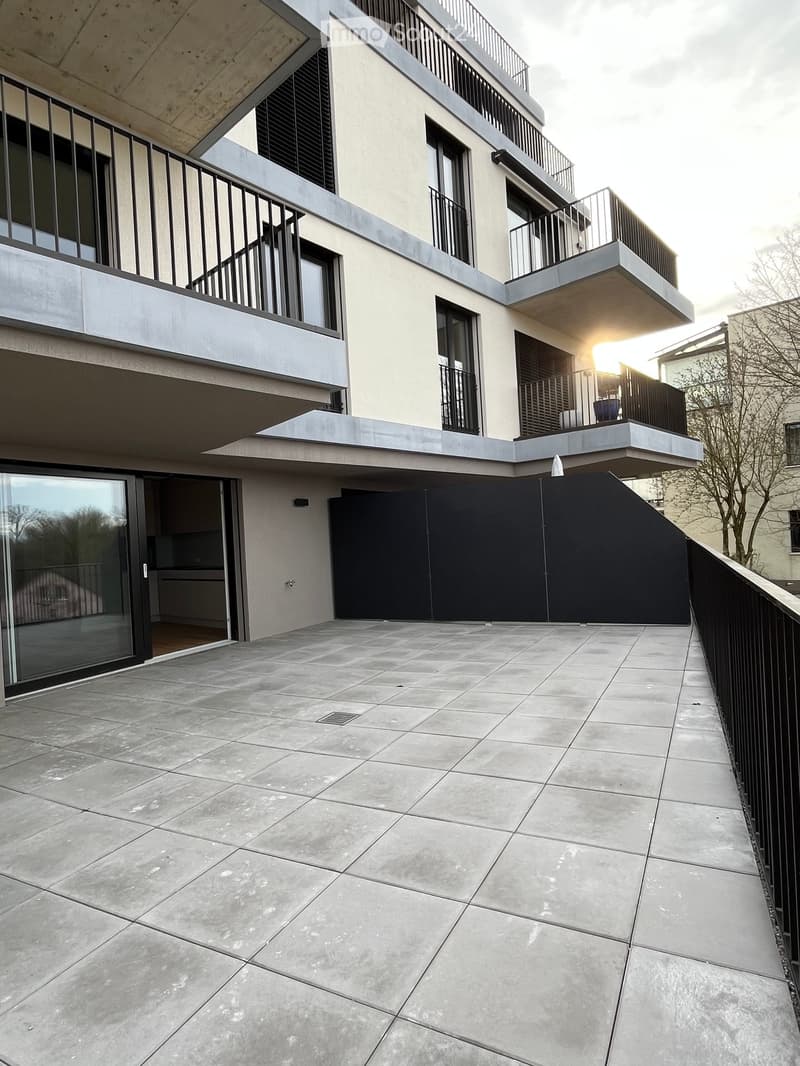 Modern balcony with concrete tiles, black metal railing, and glass door leading to interior.