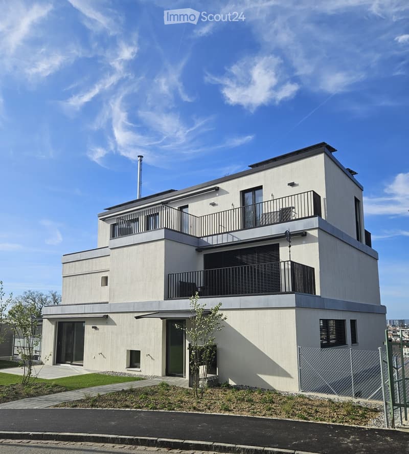 Modern two-story house with light-colored facade, large windows, and balconies on both levels.