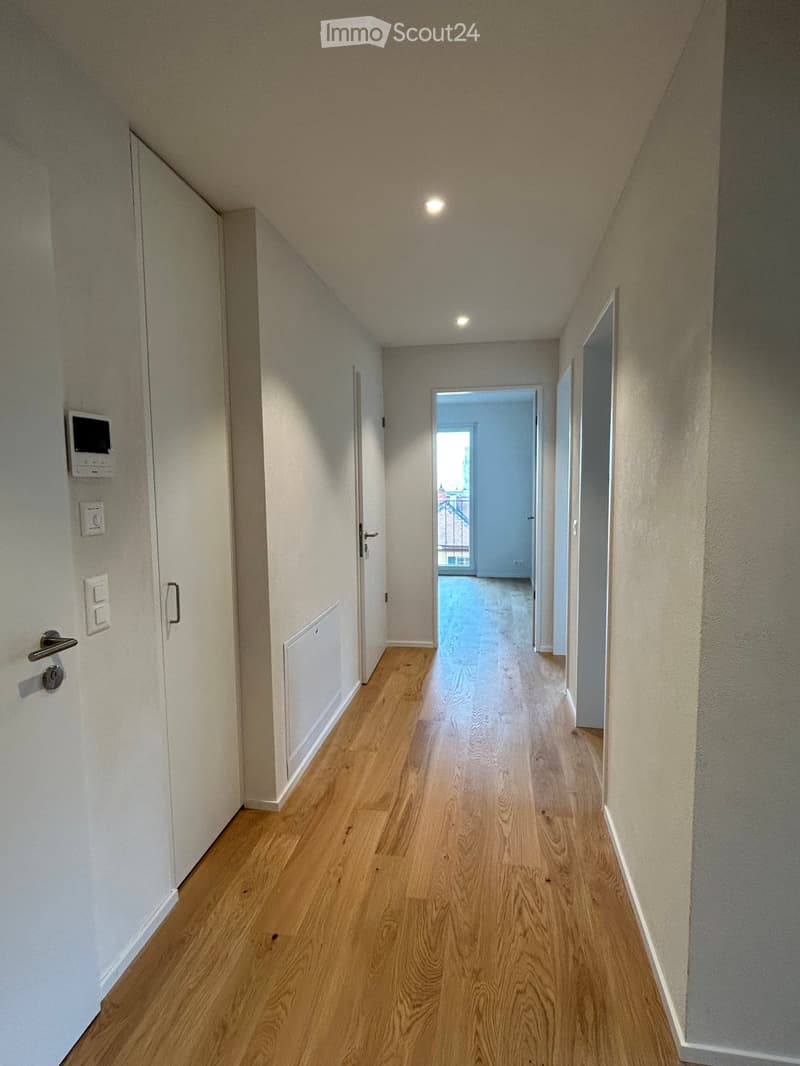 Empty hallway with wooden flooring, white walls, and several doors leading to other rooms.