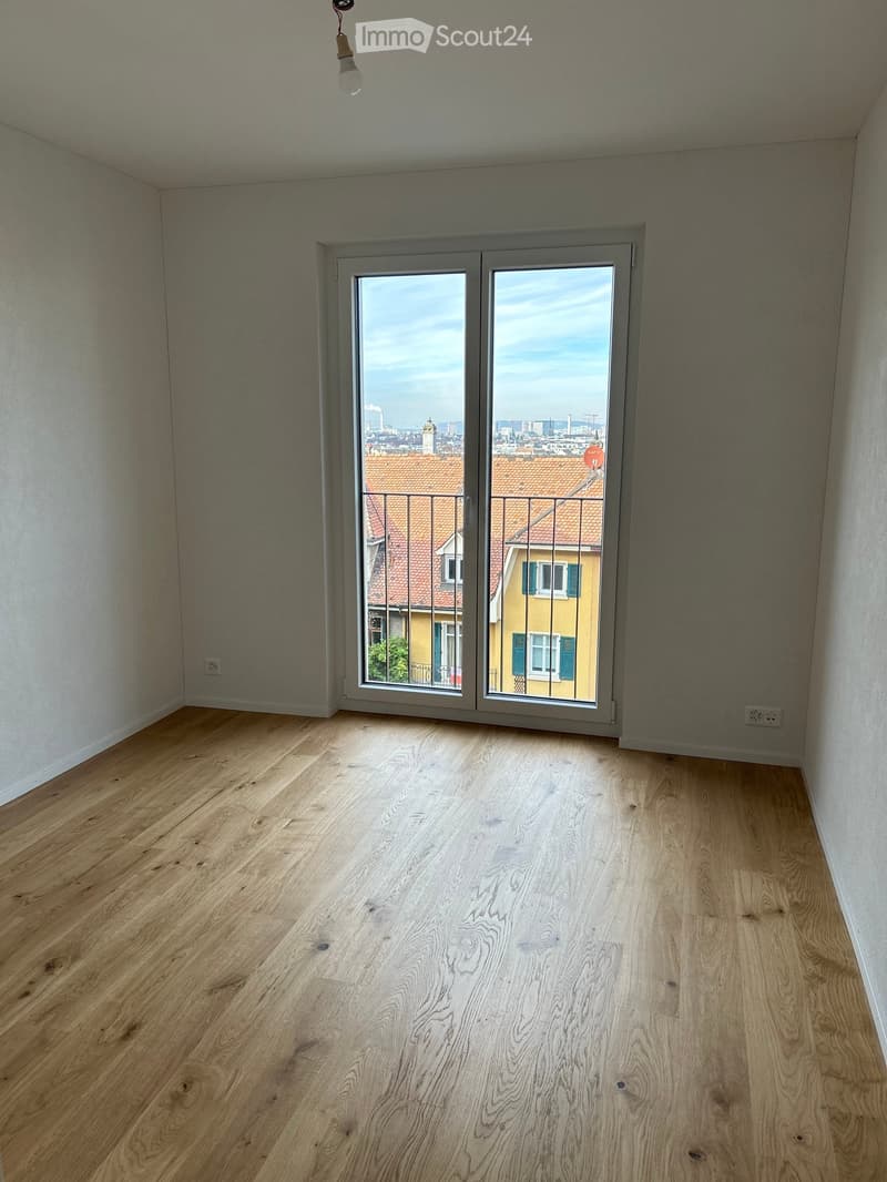 Empty room with wooden flooring and large sliding glass doors leading to a balcony with a city view.