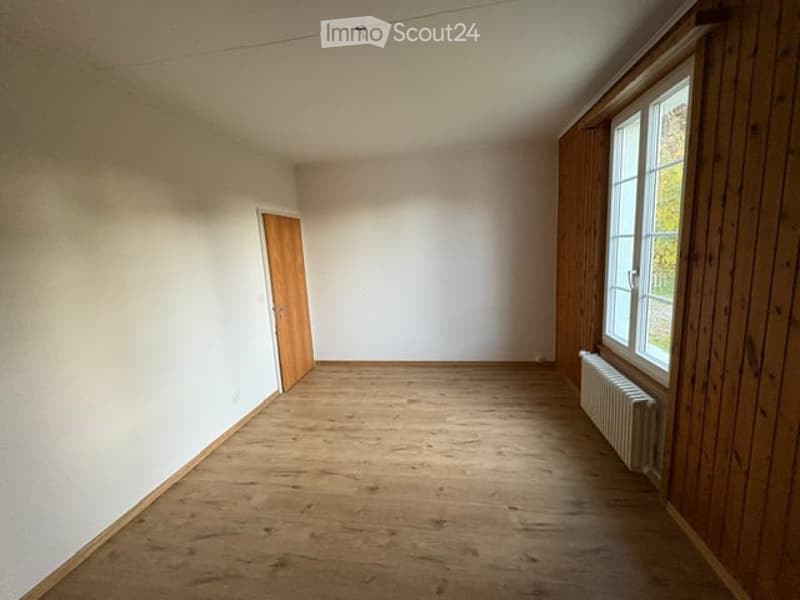 Empty room with wooden flooring, white walls, a single door, and a window with wooden frame and radiator below it.