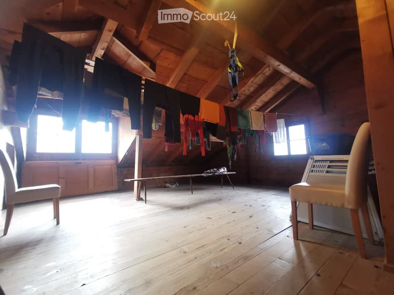 An attic space with wooden beams, wooden floor, two chairs, a small table, and clothes hanging on a line.