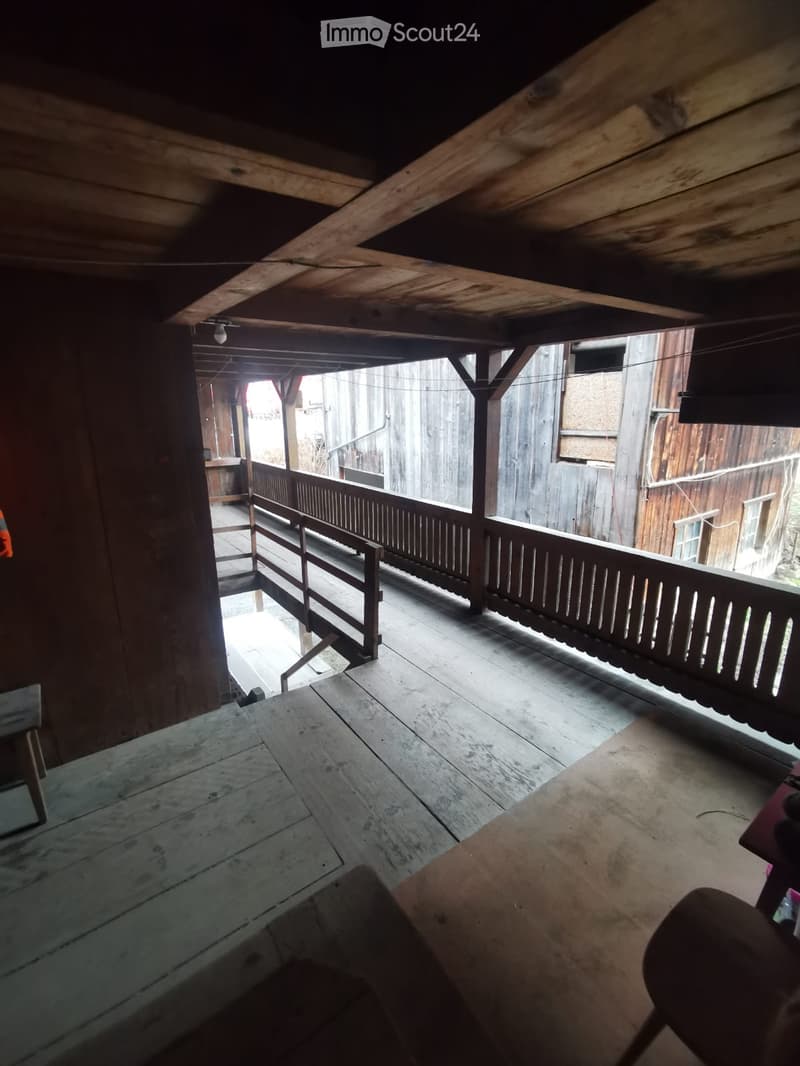 Wooden balcony with wooden railings, visible wooden beams and ceiling, and a view of the surrounding area.