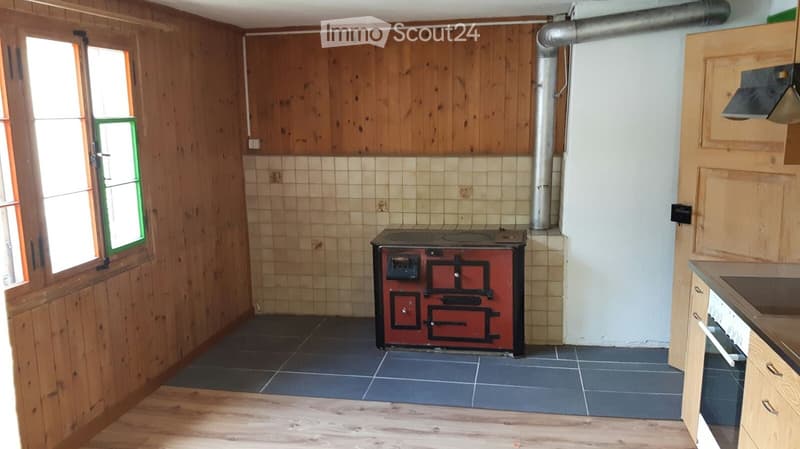 Kitchen with wooden walls, tiled lower half, dark tiled floor, and a red stove in the center.
