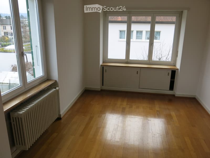 Empty room with wooden flooring, large windows, radiator, and built-in cabinetry.