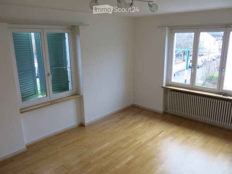 Empty room with wooden flooring, white walls, and large windows with shutters. Radiator visible under one window.