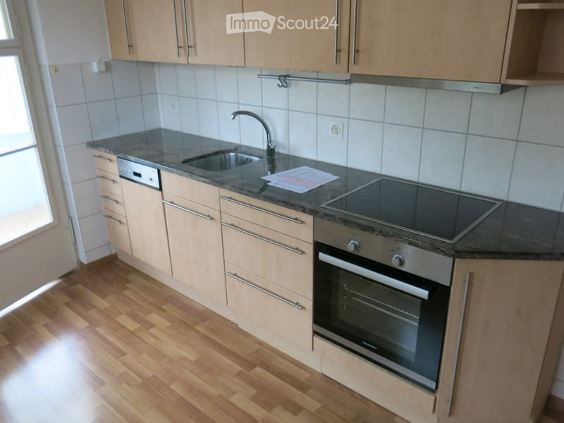 Modern kitchen with light wooden cabinets, granite countertop, stainless steel sink, faucet, oven, and dishwasher.