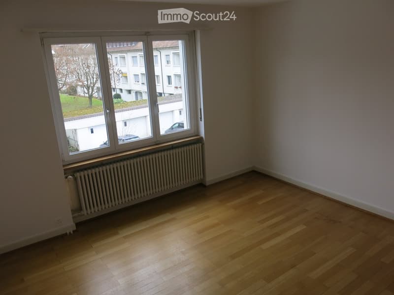 Empty room with wooden flooring, white walls, and a large window with a radiator below it.