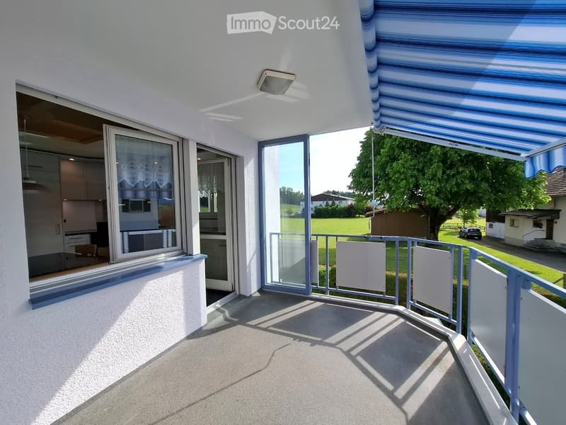 Balcony with a retractable awning, metal railing, and a view of a green lawn and trees.