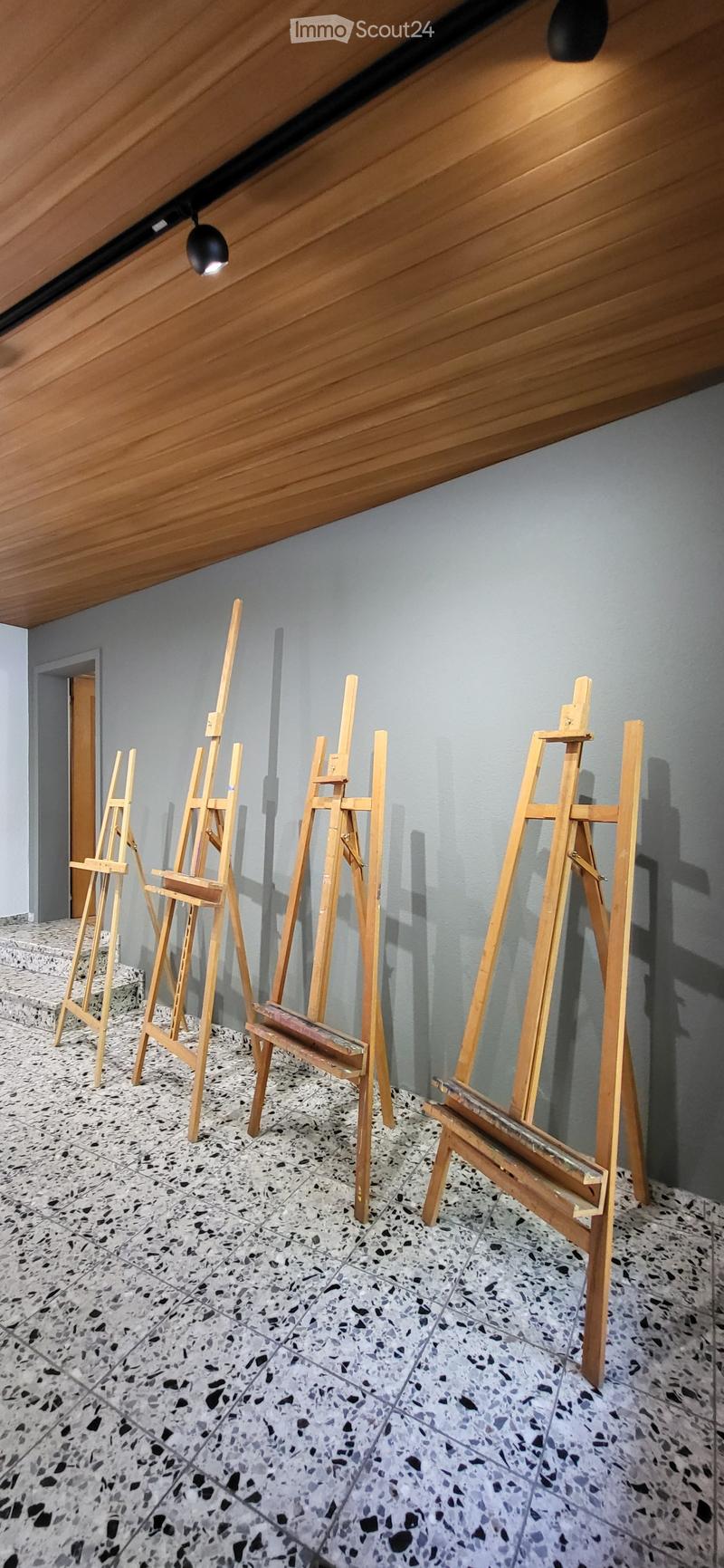 Empty room with grey walls, speckled tile floor, and wooden easels arranged in rows.