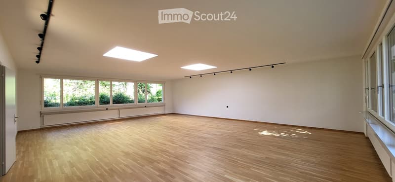 Empty room with wooden flooring, large windows, and recessed ceiling lights. No furniture or equipment present.