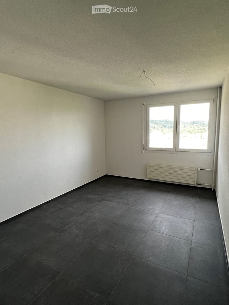 Empty room with dark tiled floor, light-colored walls, and a window with a view. A radiator is visible below the window.