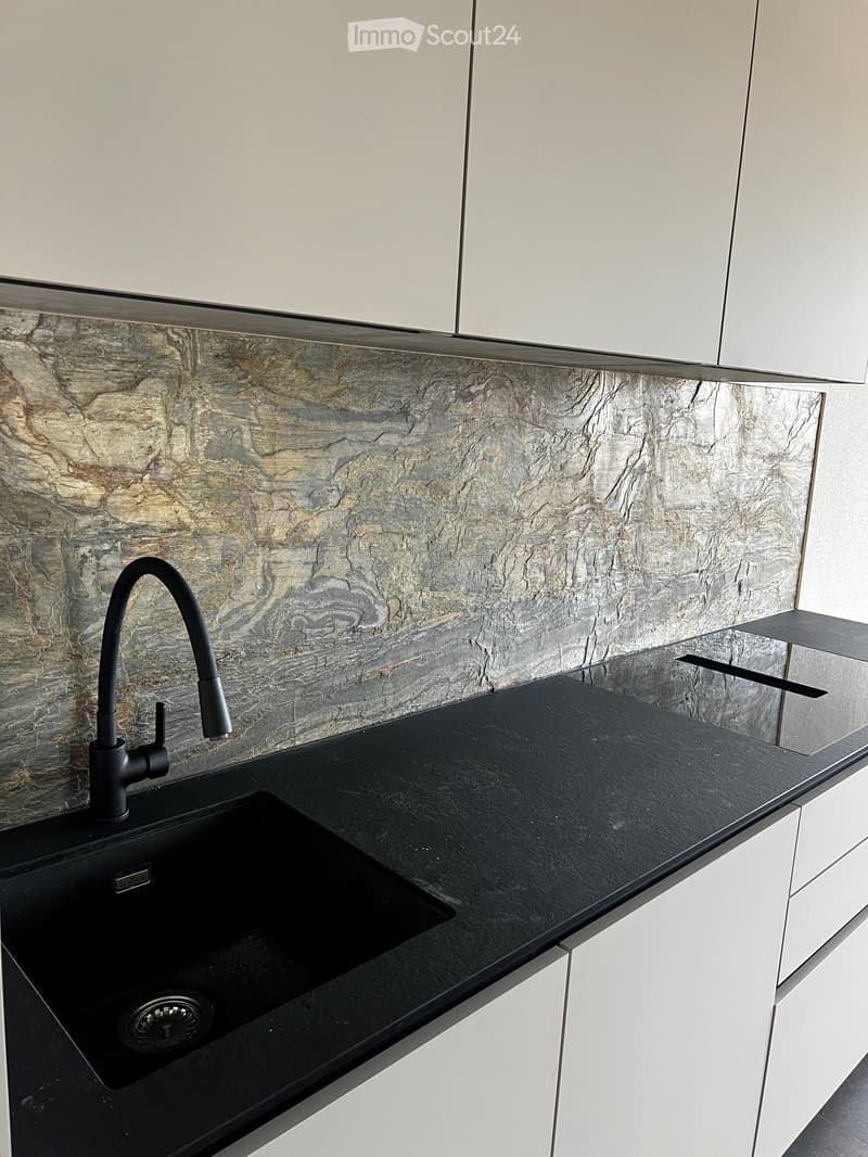 Modern kitchen with a black countertop, sleek black faucet, and a stone-textured backsplash.