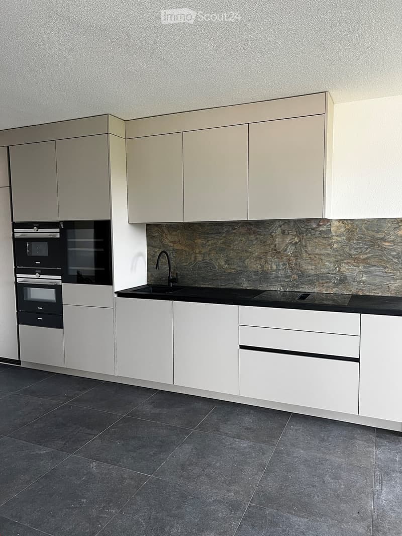 Modern kitchen with white cabinets, black countertop, and stainless steel appliances including an oven and sink.