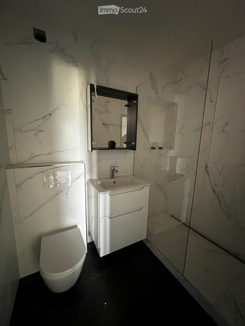 Modern bathroom with white marble walls, black tiled floor, white sink with chrome faucet, mirror, and toilet.
