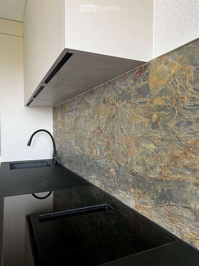 Modern kitchen with black countertops, a sleek sink, and a stylish faucet against a textured stone backsplash.