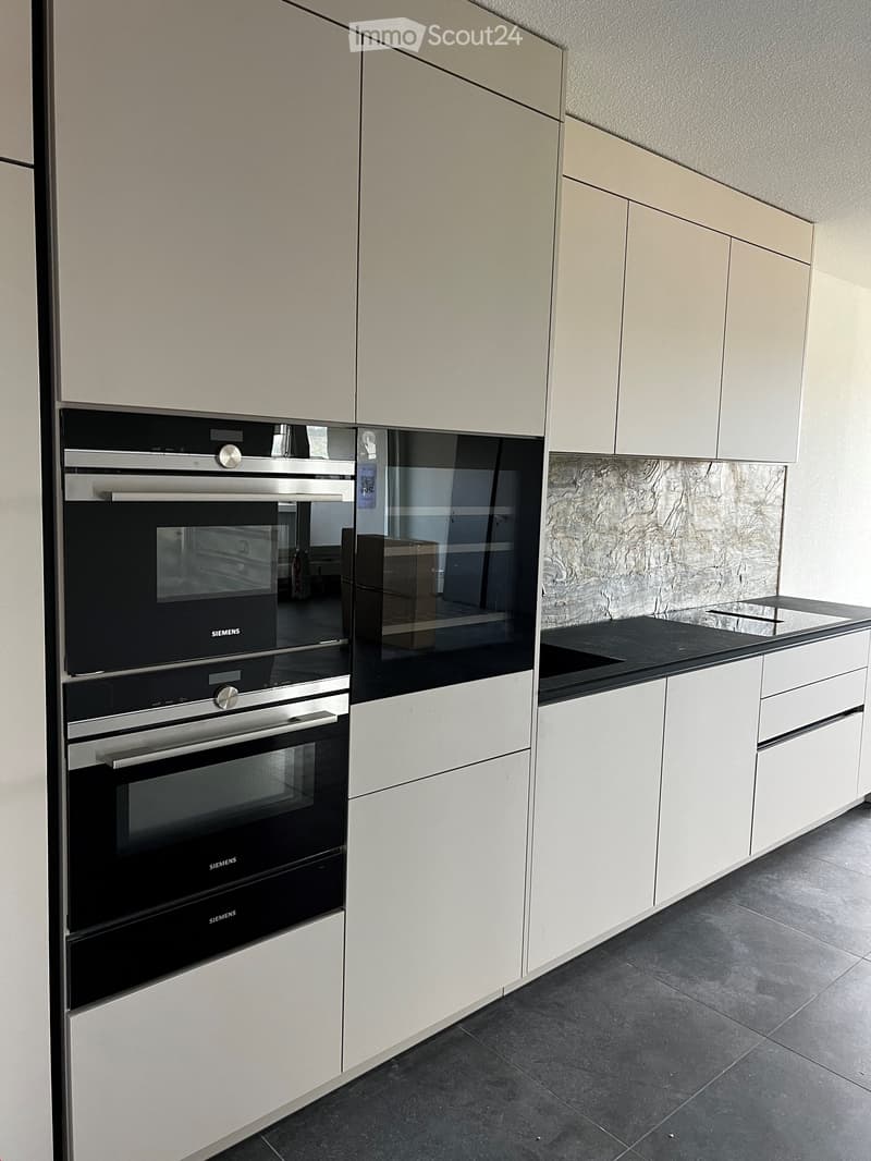 Modern kitchen with light-colored cabinets, stainless steel oven, and black countertop.