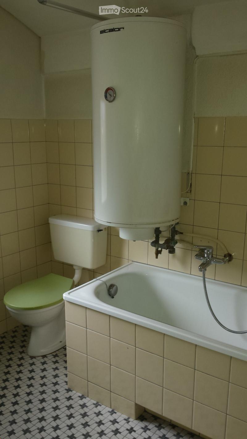 Bathroom with a toilet, bathtub, faucet, and a water heater mounted on the wall. The floor has a black and white checkered tile pattern.