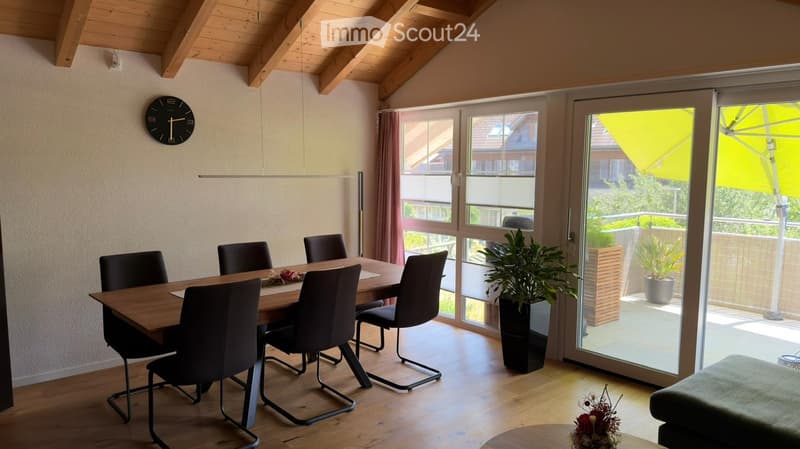 Dining room with wooden table, six chairs, clock on wall, large windows, and potted plant near sliding doors.