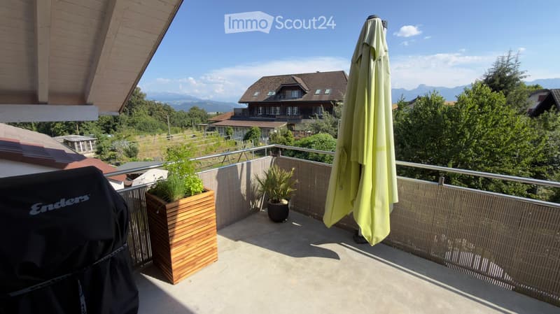 Balcony with a view of mountains and houses, featuring a closed umbrella and potted plants.