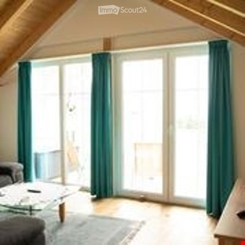 Bright living room with large windows, grey sofa, glass coffee table, laptop, and a rug on the floor.