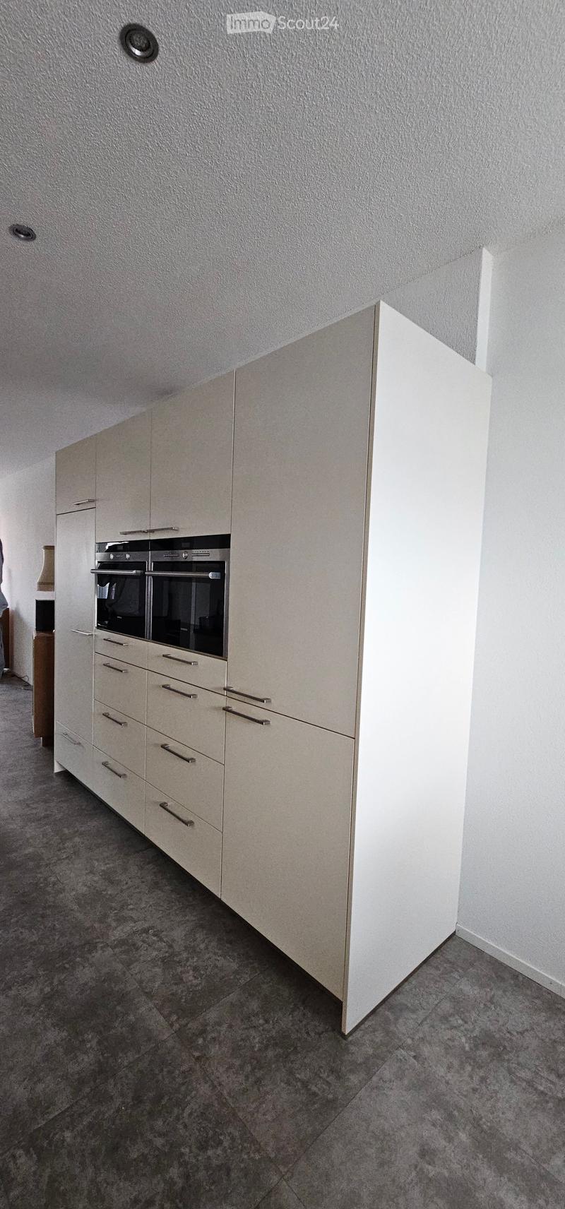 Modern kitchen with light-colored cabinets, stainless steel oven, and grey tiled floor.