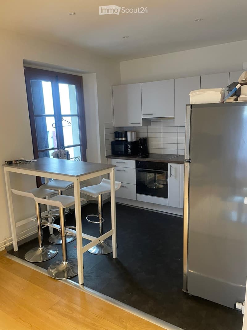 Modern kitchen with white cabinets, stainless steel appliances, a black countertop, and a small dining area with a table and four stools.