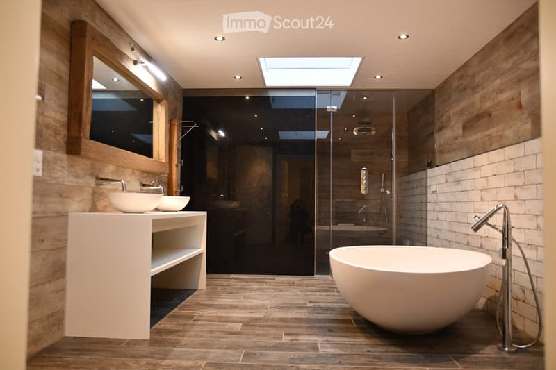 Modern bathroom with wooden walls, a large freestanding bathtub, double sink vanity, and a glass-enclosed shower area with a skylight above.