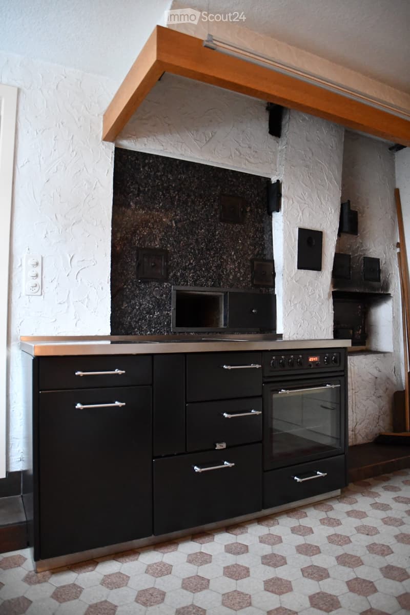 Modern kitchen with black cabinets, stainless steel oven, microwave, and countertop. The walls are textured white with a dark backsplash.