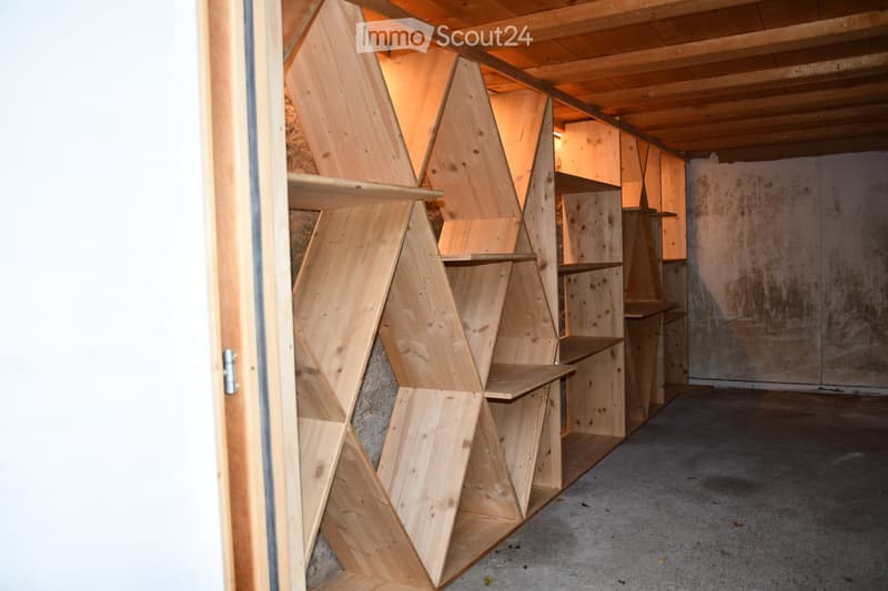 Empty room with exposed wooden beams and geometric wooden shelving units, concrete floor, and unfinished walls.