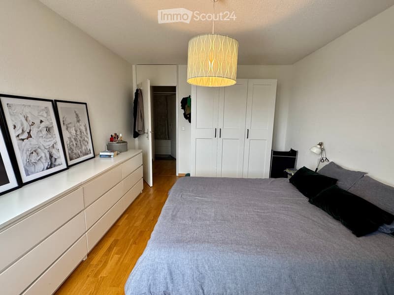 Modern bedroom with a large bed, nightstand, lamp, wardrobe, and picture frames on the wall.