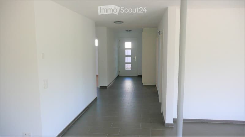 Empty hallway with white walls, dark tiled floor, and a door at the end.