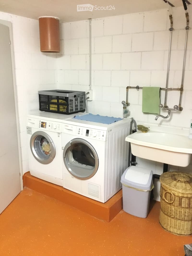 Bathroom with white brick walls, a raised floor, a washing machine, a sink, a towel, a trash bin, and a wicker basket.