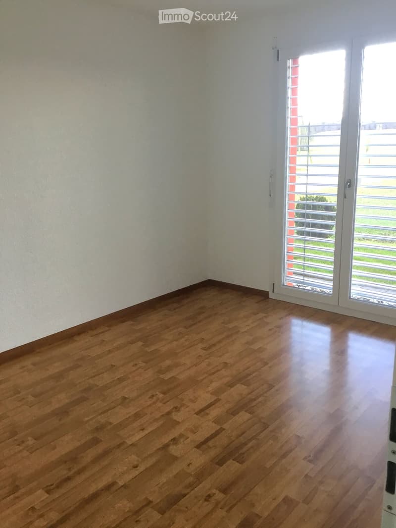 Empty room with wooden flooring and white walls, featuring a large sliding glass door leading to a balcony or outdoor area.