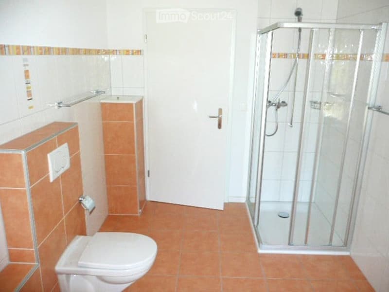 Modern bathroom with a white toilet, a glass-enclosed shower stall, a sink with a cabinet, and tiled walls and floor in warm tones.