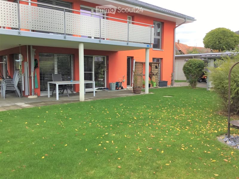 Garden area with green lawn, scattered leaves, patio furniture, and a balcony with white balustrade.